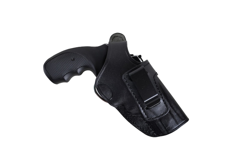 May include: Black leather holster with a black revolver. The holster features a belt clip and is designed to securely hold the firearm. The revolver has a textured grip for a secure hold.