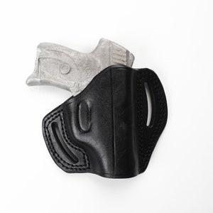 May include: A black leather holster with a silver handgun partially inserted. The holster has a molded design with stitched edges and belt loops. The handgun's grip is visible, contrasting with the holster's dark color. The background is plain white.