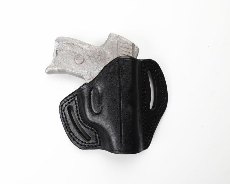 May include: A black leather holster with a silver handgun partially inserted. The holster has a molded design with stitched edges and belt loops. The handgun's grip is visible, contrasting with the holster's dark color. The background is plain white.