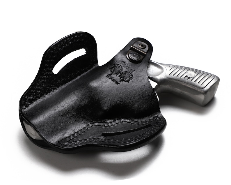 Puede incluir: Funda de cuero negra con un rev&oacute;lver plateado en su interior. La funda tiene un bucle para el cintur&oacute;n y un cierre a presi&oacute;n. El rev&oacute;lver tiene un acabado plateado y una empu&ntilde;adura negra.