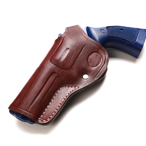 Könnte beinhalten: Eine braune Lederholster mit einer blauen Schusswaffe. Die Holster ist ein sattes, dunkles Braun mit sichtbaren Nähten und einem genieteten Design. Der blaue Griff der Schusswaffe kontrastiert mit der Farbe der Holster.