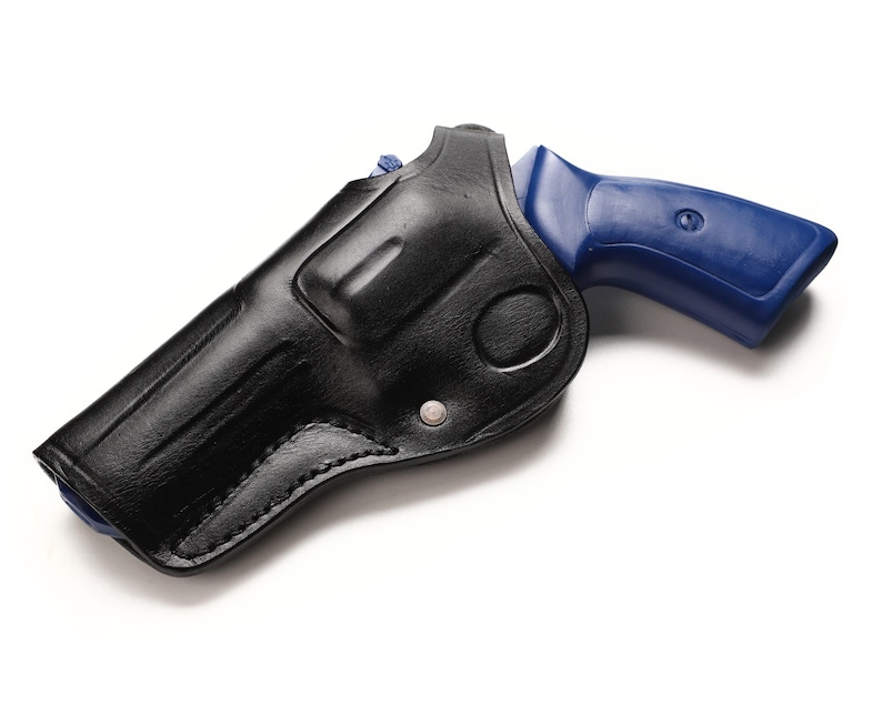 May include: A black leather holster with a silver rivet holds a blue-handled revolver. The holster is molded to the shape of the gun, with visible stitching along the edges. The background is plain white.