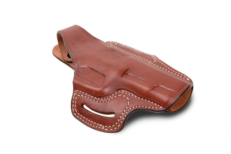May include: A brown leather holster with white stitching. The holster has a belt loop and a trigger guard.