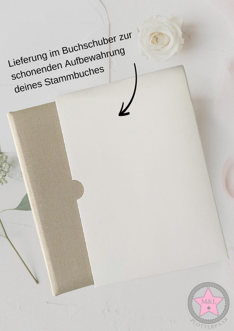 May include: A white book with a beige slipcover. The book is closed and the slipcover is folded over the top. The text on the slipcover reads "Lieferung im Buchschuber zur schonenden Aufbewahrung deines Stammbuches".
