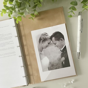 May include: A black and white photograph of a couple looking at each other. The photo is in a brown photo album with a white background.