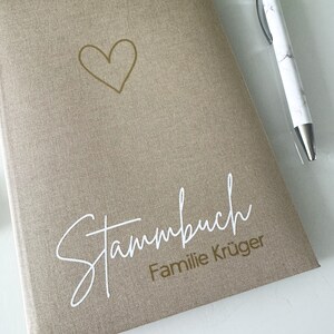 May include: A beige linen-textured journal with a gold heart and the text "Stammbuch Familie Kr&uuml;ger" in white lettering.
