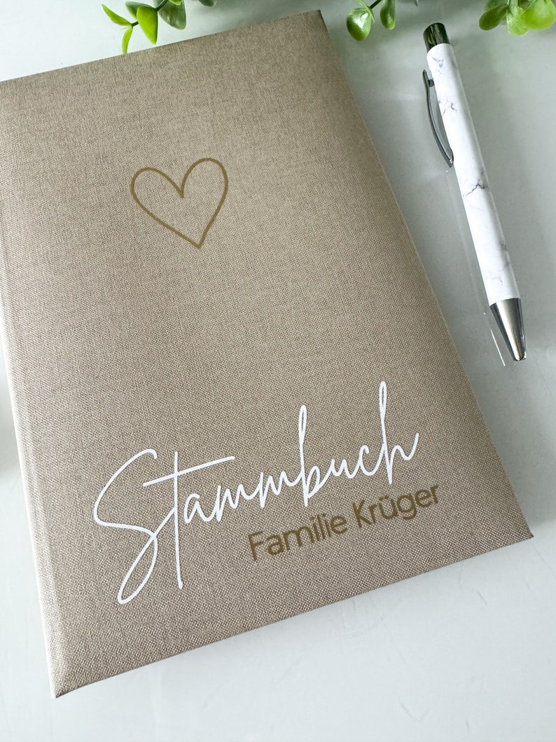 May include: A beige linen-textured journal with a gold heart and the text "Stammbuch Familie Kr&uuml;ger" in white lettering.