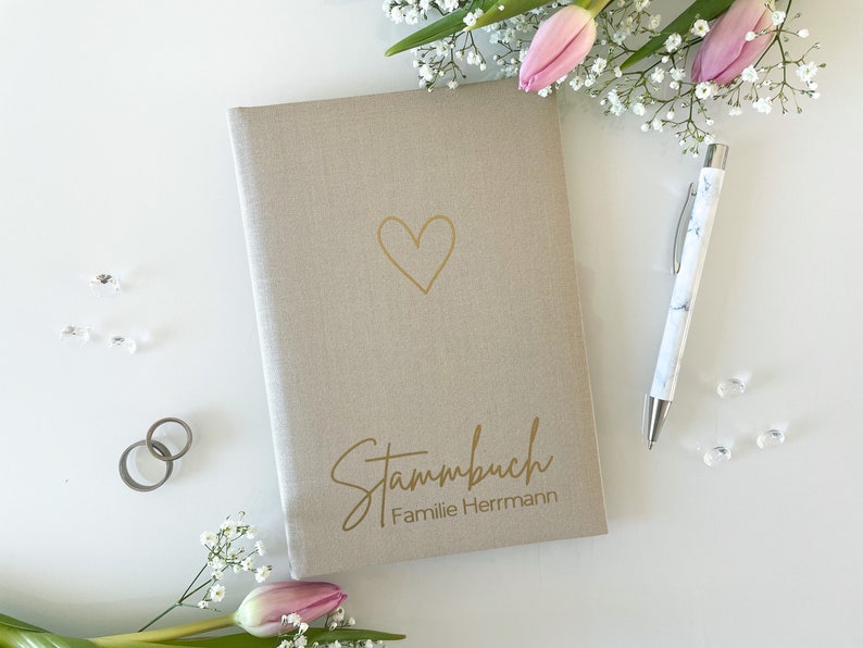 May include: A beige linen-covered journal with a gold heart and the text "Stammbuch Familie Herrmann" on the front.