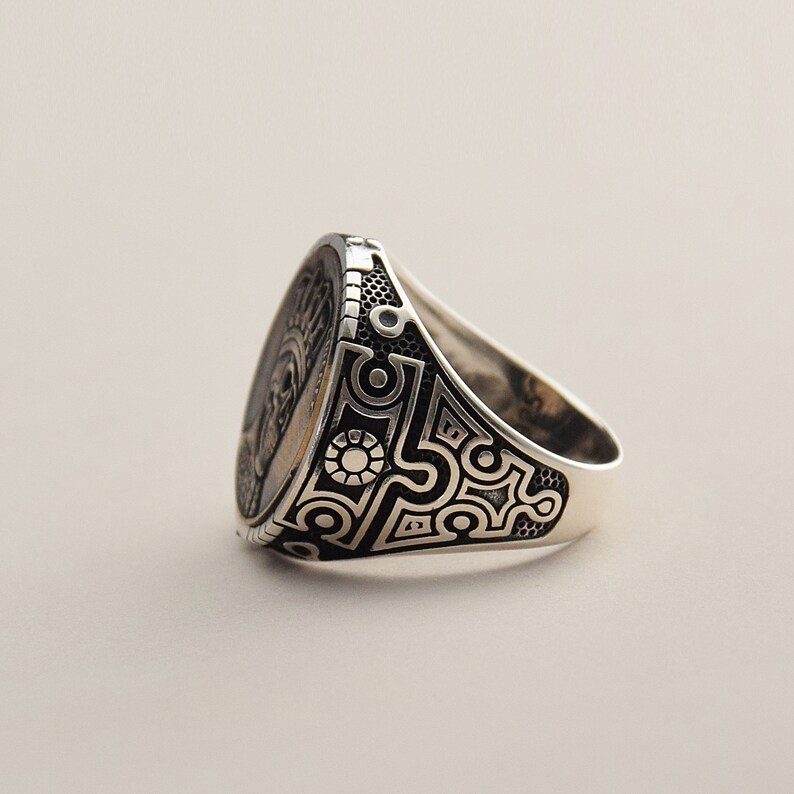 May include: A silver ring with a black and white geometric design. The ring has a large oval face with a detailed design.