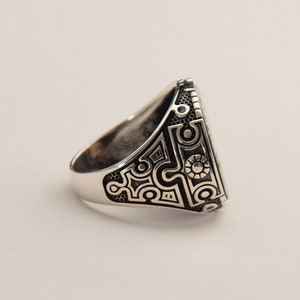 May include: A silver ring with a detailed geometric design on the band. The design is black and silver and has a circular pattern.