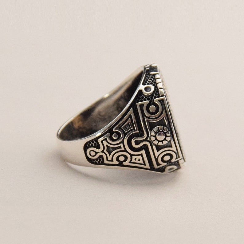 May include: A silver ring with a detailed geometric design on the band. The design is black and silver and has a circular pattern.