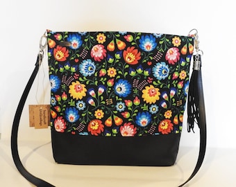 May include: Black tote bag with a floral print featuring colorful flowers on a black background. The bag has a black leather bottom and a black tassel.