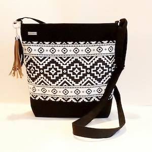 Peut inclure: Sac à bandoulière en toile noire avec un motif géométrique blanc. Le sac a une longue bandoulière réglable et un charme en forme de pompon.