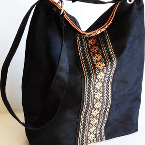 May include: Black canvas tote bag with a long strap and a decorative embroidered panel featuring geometric patterns in orange, brown, and blue.