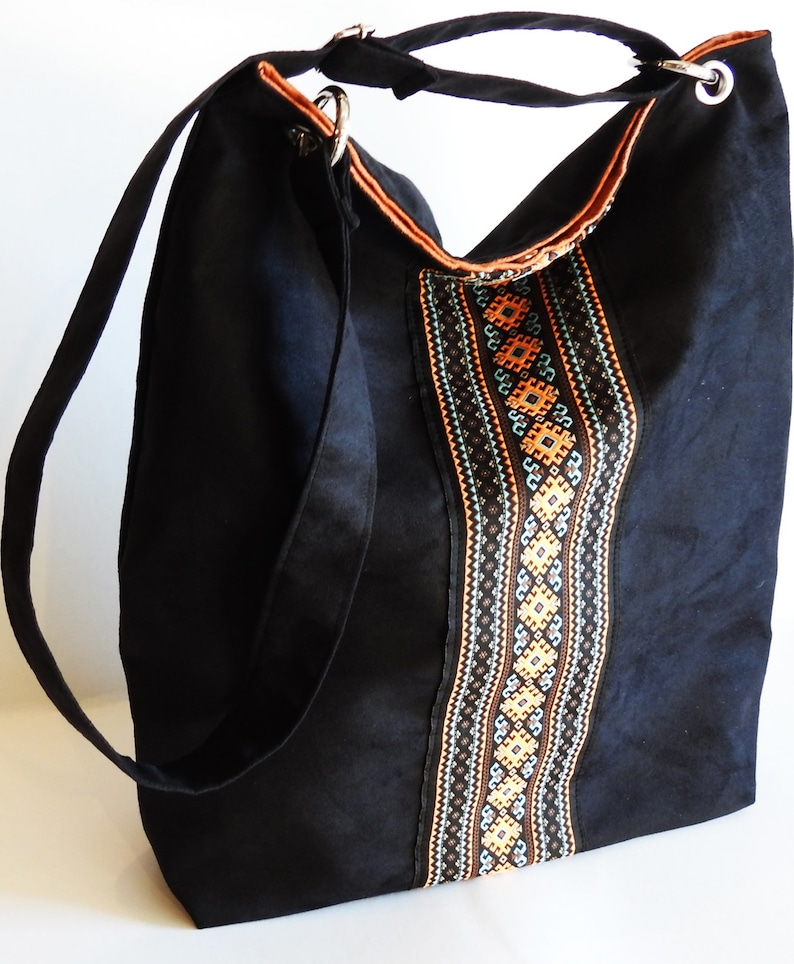 May include: Black canvas tote bag with a long strap and a decorative embroidered panel featuring geometric patterns in orange, brown, and blue.