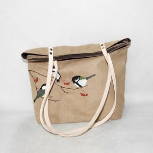 May include: A brown canvas tote bag with white straps and a painted design of three birds on a branch with red berries.