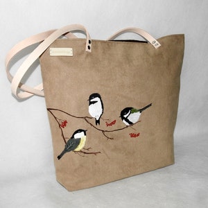 May include: A brown canvas tote bag with leather straps and a UniqueBags label. The bag features an embroidered design of four birds perched on a branch with red berries.