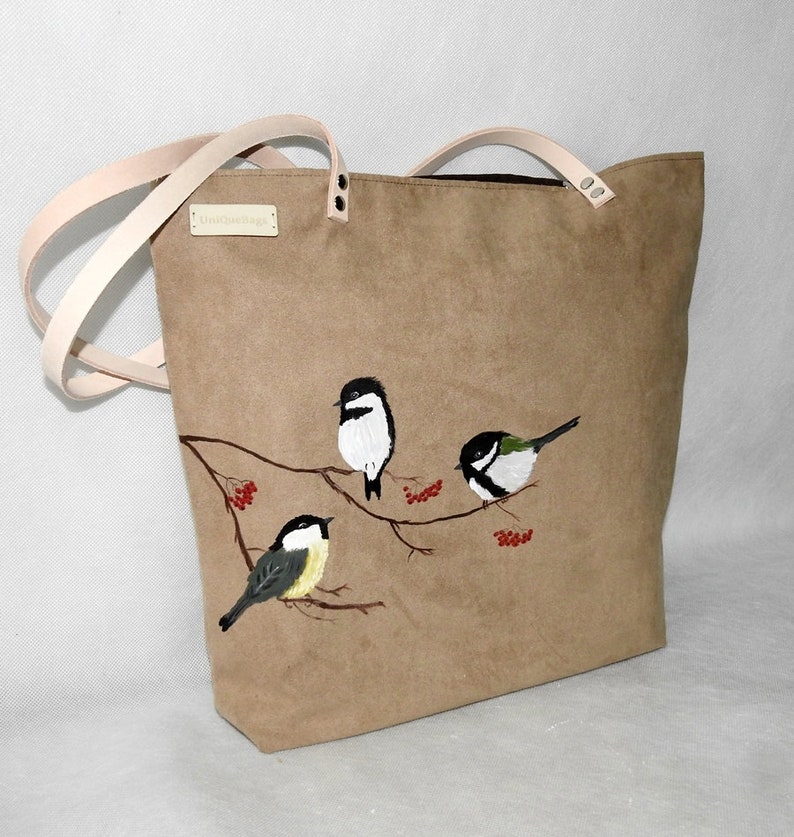 May include: A brown canvas tote bag with leather straps and a UniqueBags label. The bag features an embroidered design of four birds perched on a branch with red berries.