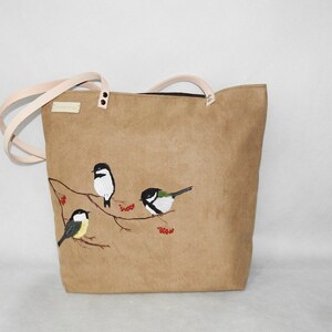 May include: A brown canvas tote bag with a design of four birds on a branch with red berries. The birds are painted in black, white, and green.