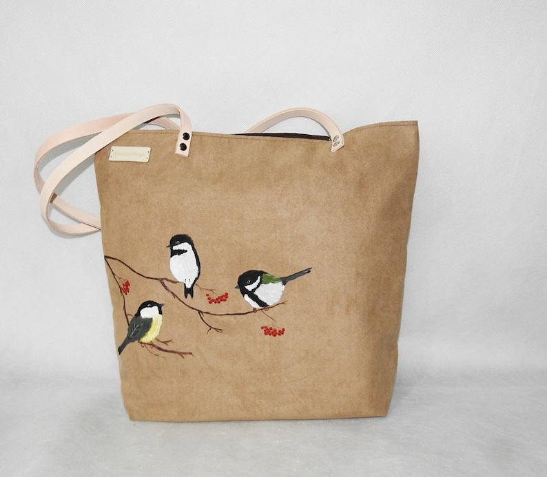 May include: A brown canvas tote bag with a design of four birds on a branch with red berries. The birds are painted in black, white, and green.