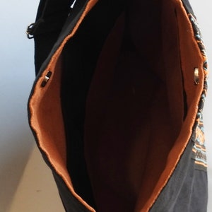 May include: Black canvas tote bag with a brown lining and a colorful geometric pattern on the side. The bag has two silver D-rings on the top.