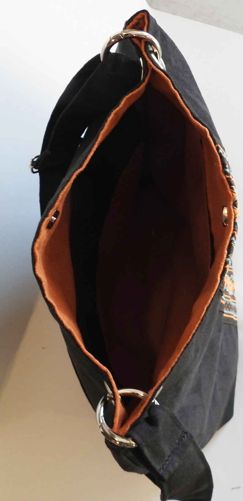 May include: Black canvas tote bag with a brown lining and a colorful geometric pattern on the side. The bag has two silver D-rings on the top.