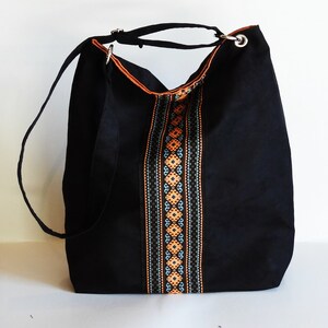 May include: Black canvas tote bag with a long strap and a colorful embroidered design down the center.