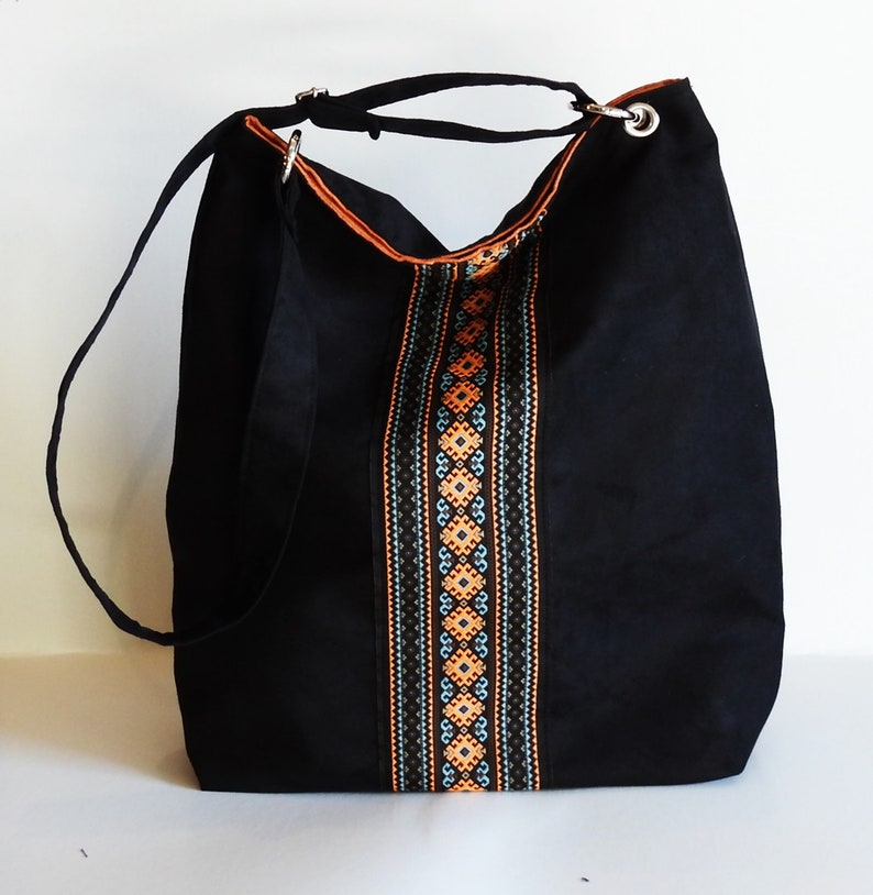 May include: Black canvas tote bag with a long strap and a colorful embroidered design down the center.