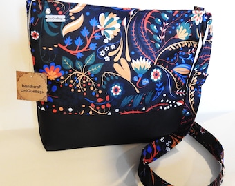 May include: A black crossbody bag with a floral print featuring colorful flowers and leaves on a black background. The bag has a black strap and a brown tag that reads "handicraft UniQueBags".