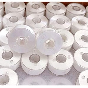 May include: A close-up of a large quantity of white plastic bobbins for sewing machines.