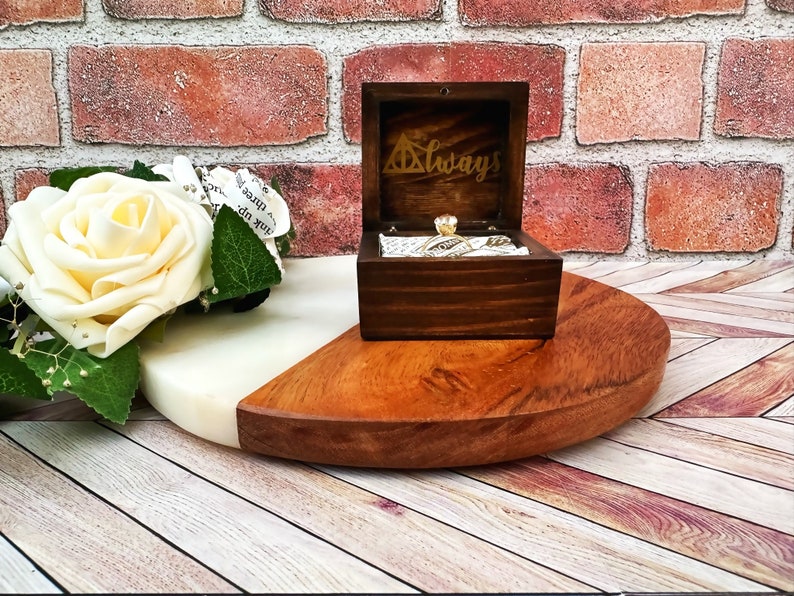 A wooden ring box or a wooden jewelry box stained in a rich espresso color, with gold vinyl saying Always. A cushion is wrapped in wizard sport fabric where a ring or necklace can sit. There are built in barrel hinges and a magnetic latch.