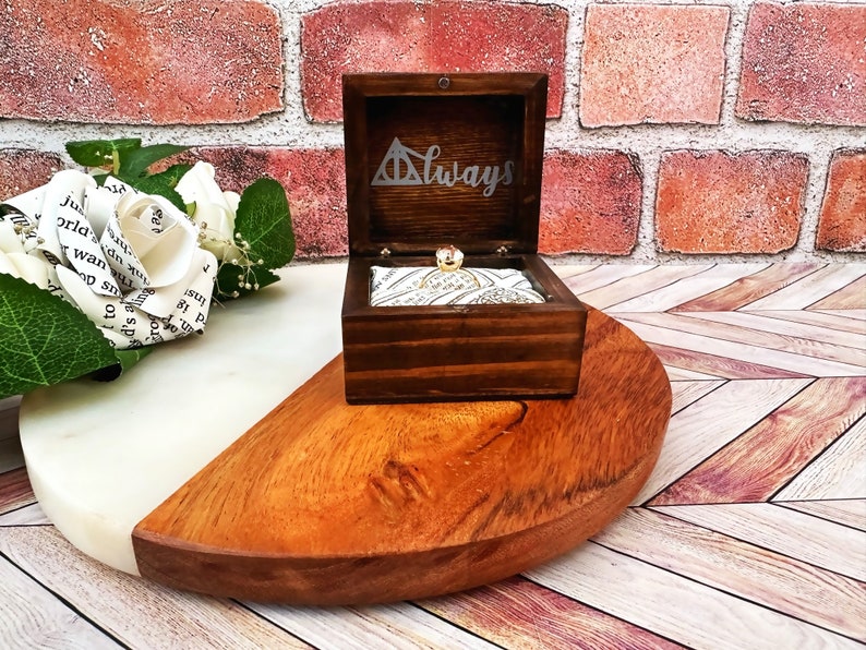 A wooden ring box or a wooden jewelry box stained in a rich espresso color, with silver vinyl saying Always. A cushion is wrapped in wizard sport fabric where a ring or necklace can sit. There are built in barrel hinges and a magnetic latch.