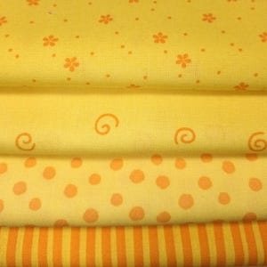 Könnte beinhalten: Ein Stapel gelber Stoffmuster mit verschiedenen Mustern. Die Muster umfassen kleine orangefarbene Blumen, Punkte, Wirbel und vertikale Streifen. Der Stoff hat ein weiches, strukturiertes Aussehen.