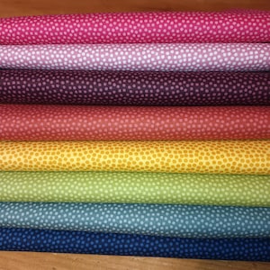 Könnte beinhalten: Ein Stapel von sieben Stoffproben mit einem Tupfenmuster. Die Proben sind in einer Regenbogenfarbenfolge angeordnet, beginnend mit Pink und endend mit Blau.