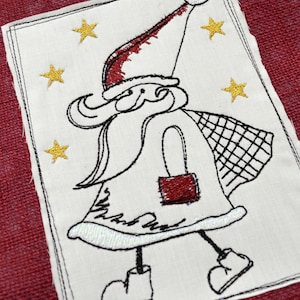 Pode incluir: Remendo de tecido branco bordado com um desenho de Papai Noel preto e vermelho. O Papai Noel está usando um chapéu vermelho e carregando uma bolsa vermelha. O fundo é branco com estrelas douradas.