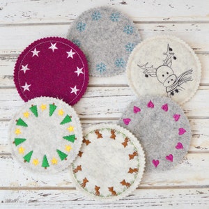 Peut inclure: Six dessous-de-verre ronds en feutre avec différents motifs brodés. Les dessous-de-verre sont blancs, gris et bordeaux avec des broderies blanches, vertes, brunes et roses. Les motifs comprennent des flocons de neige, un renne, des sapins, des cœurs et des cerfs.