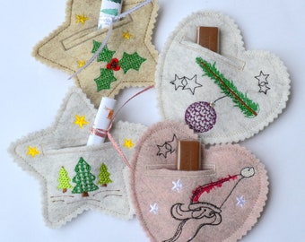 May include: Four felt Christmas decorations, two stars and two hearts, with embroidered designs and pockets for small gifts. The decorations are beige, white, and pink.