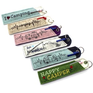 May include: Six colorful felt keychains with different designs and text. The designs include a heart with the word "Camping", a camper van with a heartbeat, a fishing rod with the word "Angeln", a camper van with a heartbeat, and the words "Happy Camper".