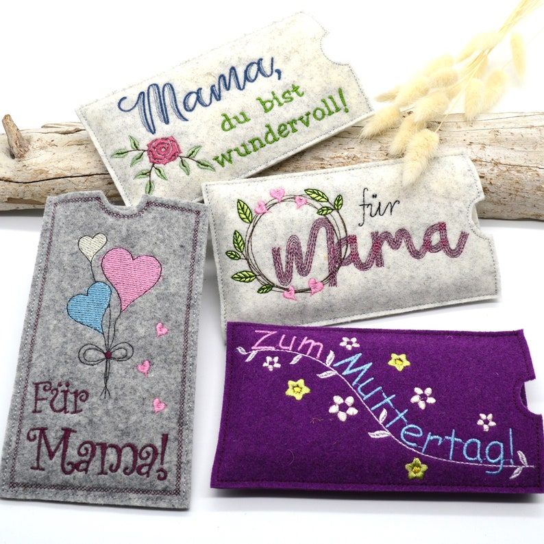 May include: Four felt phone cases with embroidered designs for Mother's Day. The cases are in gray, white, and purple with different embroidery designs including hearts, flowers, and the word "Mama".