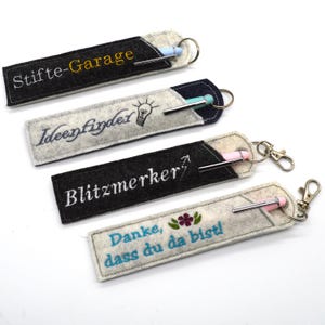 Peut inclure: Quatre porte-stylos en feutre avec différents motifs brodés et porte-clés. Les motifs comprennent "Stifte-Garage", "Ideenfinder", "Blitzmerker" et "Danke, dass du da bistl".