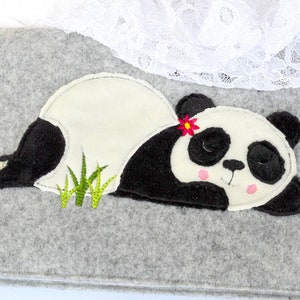 May include: A black and white embroidered panda bear with a pink flower on its head, lying down on a gray felt background.
