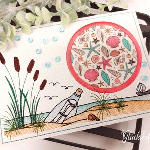 May include: Embroidered postcard with a seashell design in a red circle, a bottle with a message in the sand, and cattails on the left side. The postcard has a white background and blue stitching around the edges.