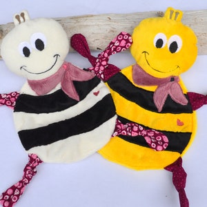 Puede incluir: Dos juguetes de peluche de abeja con rayas blancas y negras y detalles de lunares rosas. Una abeja es amarilla y la otra es blanca.