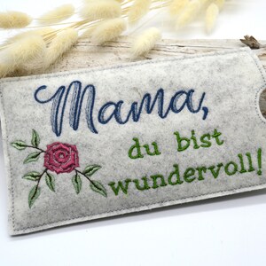 May include: A gray felt pouch with a white embroidered rose and the text "Mama, du bist wundervoll!" in green and blue thread.