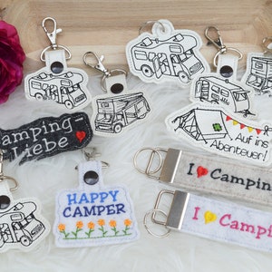 May include: A collection of keychains featuring camping-themed designs. The keychains are made of felt and feature various designs, including a camper van, a tent, and the phrase "I love camping".