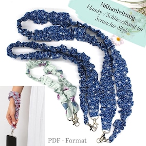 May include: A collection of fabric lanyards in scrunchie style, featuring a dark blue strap with a white geometric star pattern and a light green strap with a floral print. Each strap includes a silver metal swivel clasp for attachment.