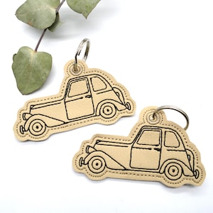May include: Two tan leather keychains with black embroidered vintage car designs. Each keychain has a silver metal key ring.