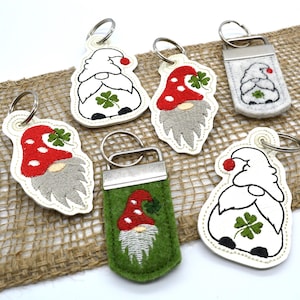 May include: Five different gnome-themed keychains with a red and white hat, a green shamrock, and a white beard. The keychains are made of felt and have a silver metal ring.