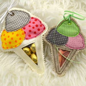 Puede incluir: Dos bolsas de tela con forma de cono de helado con parches de tela de diferentes colores. Una bolsa tiene un parche de tela amarillo, rosa y marrón y la otra tiene un parche de tela verde, rosa y marrón. Ambas bolsas tienen una ventana de plástico transparente para ver el contenido en el interior.