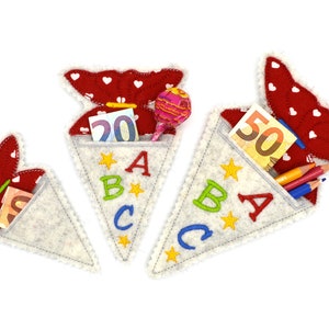 Könnte beinhalten: Drei kegelförmige Schultüten aus Filz in Weiß und Rot. Die Tüten haben die Buchstaben A, B und C und sind mit Sternen verziert. Eine Tüte enthält einen Lolli, eine andere Geld und die dritte Stifte.